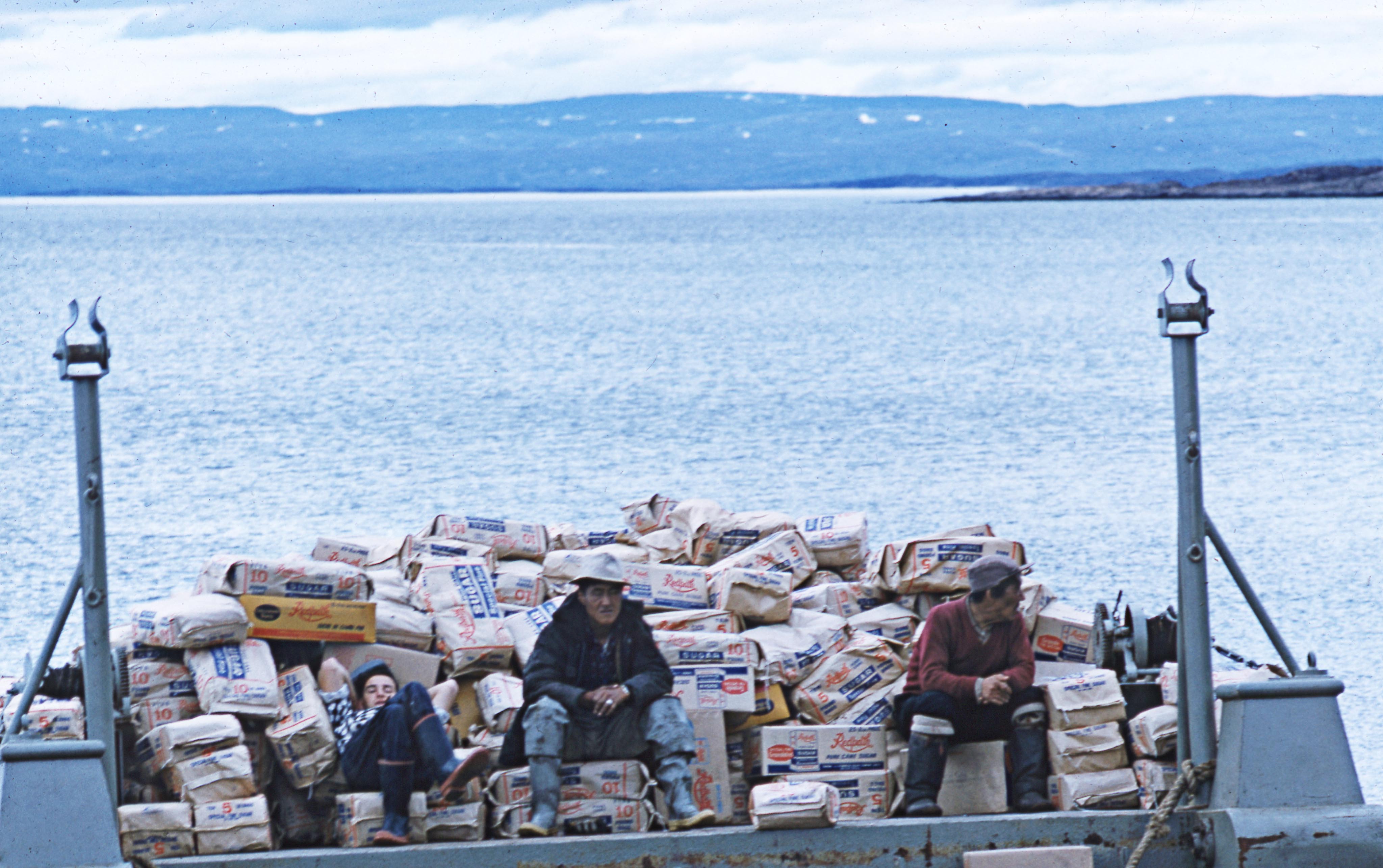 Three males sitting on a barge full of bags of sugar